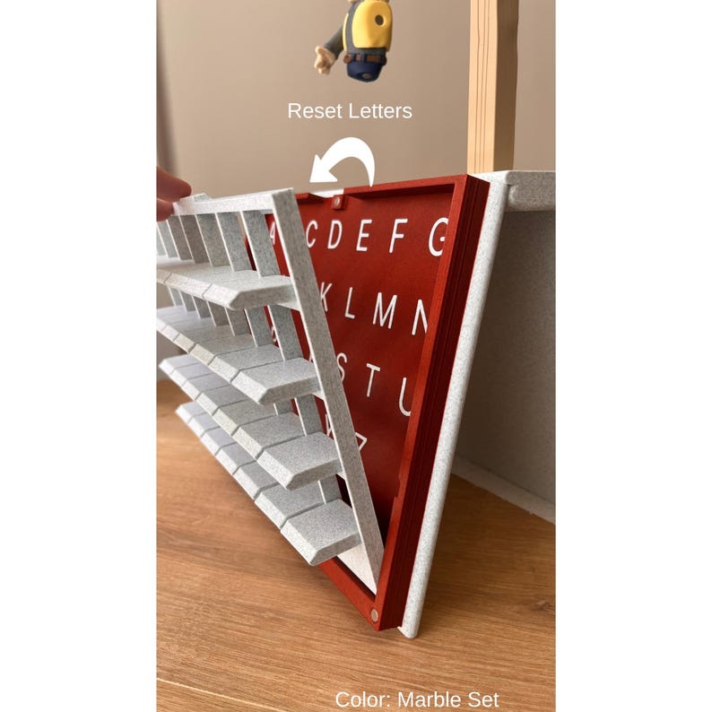 May include: A red and white marble-effect alphabet board with grey letter tiles. The board displays the letters C, D, E, F, G, K, L, M, N, S, T, and U. The text "Reset Letters" is above the board.