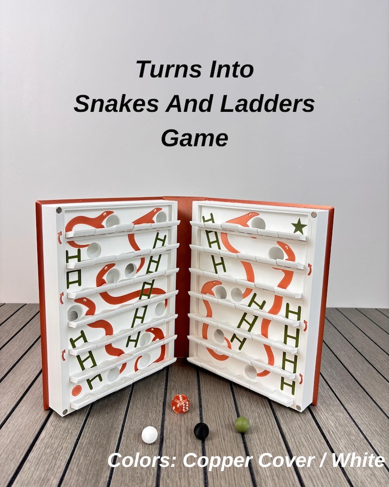 May include: A board game titled Turns Into Snakes And Ladders Game with a copper cover and white interior. The game board features orange snakes, green ladders, and circular holes. Included are one red die and three small spheres in white, black, and green.