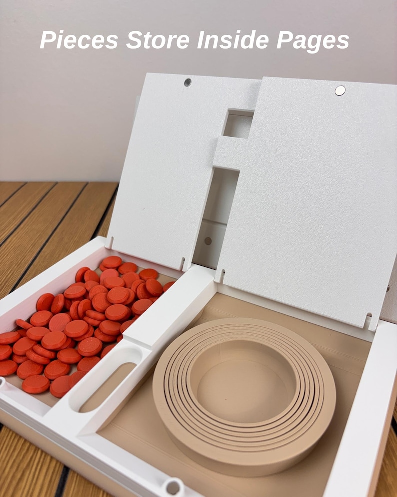 May include: A white storage organizer with the text Pieces Store Inside Pages. The left compartment contains numerous small, round, orange game pieces. The right compartment holds a set of nested, circular, beige rings of varying sizes.