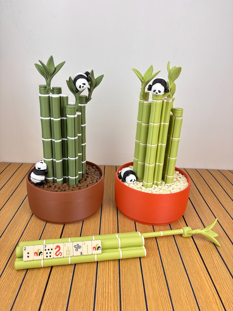 May include: Two decorative planters shaped like bamboo stalks with small panda figures. One planter is brown with dark soil, the other is orange with white pebbles. A separate bamboo stalk piece lies horizontally with mahjong tiles attached.