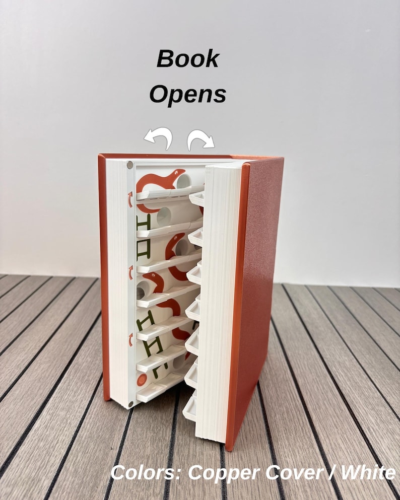 May include: A copper-colored book with a white interior storage system. The book opens to reveal white shelves featuring orange snake graphics and small white circular cutouts. Text above the book reads Book Opens, and text below reads Colors: Copper Cover / White.