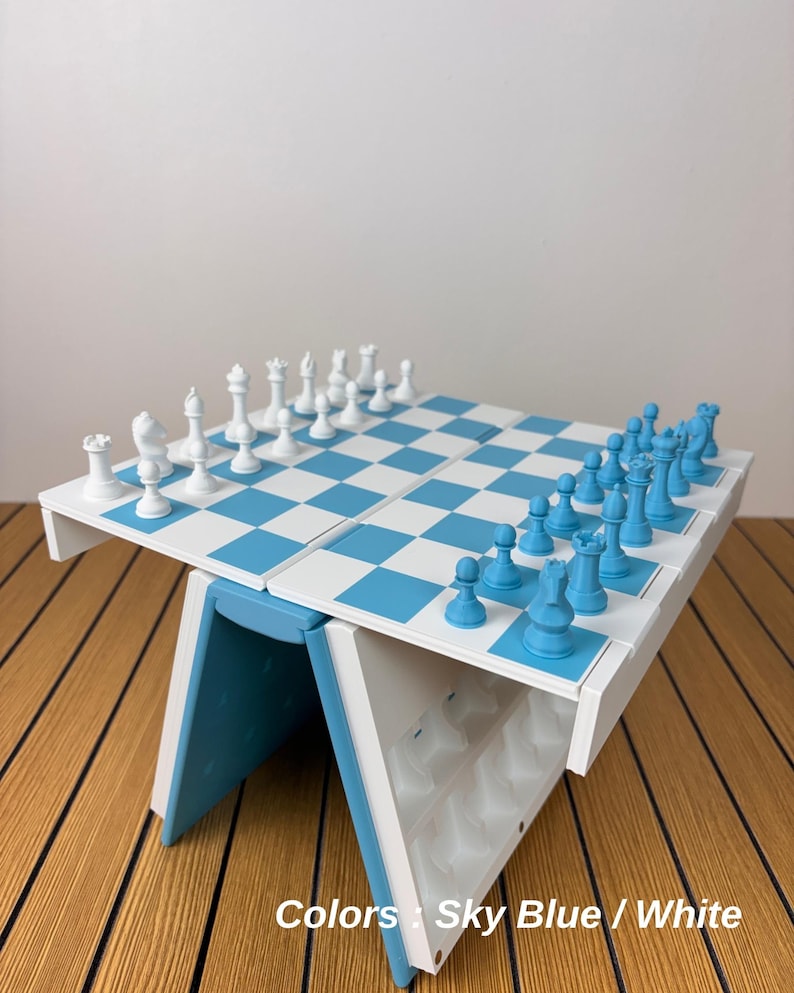 K&ouml;nnte beinhalten: Ein klappbares Schachspiel mit einem Spielbrett im hellblauen und wei&szlig;en Schachbrettmuster. Das Set enth&auml;lt einen vollst&auml;ndigen Satz wei&szlig;er und hellblauer Schachfiguren, die auf dem Brett angeordnet sind. Der Sockel ist wei&szlig; und hellblau.