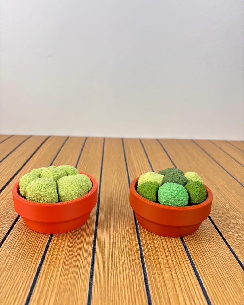 Puede incluir: Dos macetas peque&ntilde;as y redondas de terracota naranja, cada una con un grupo de plantas suculentas artificiales texturizadas, redondeadas, de color verde claro y oscuro. Las plantas tienen una superficie rugosa y compacta.