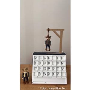 May include: A navy blue alphabet letter board with a cowboy figure hanging from a wooden gallows. A second cowboy figure stands beside the board. The board has white letter tiles and the text "Color: Navy Blue Set".