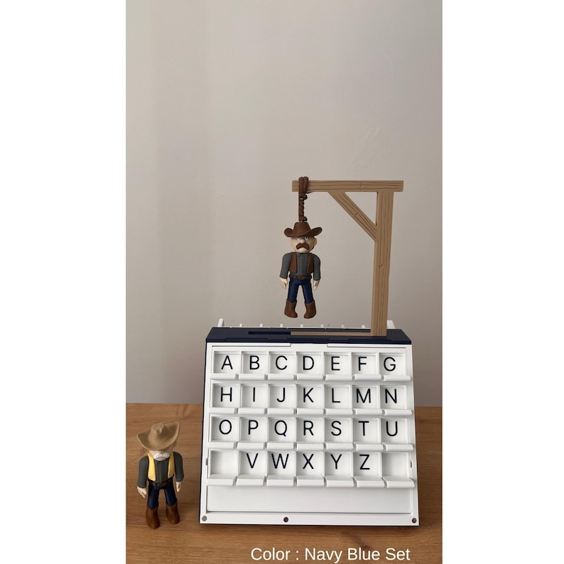 May include: A navy blue alphabet letter board with a cowboy figure hanging from a wooden gallows. A second cowboy figure stands beside the board. The board has white letter tiles and the text "Color: Navy Blue Set".
