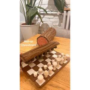 K&ouml;nnte beinhalten: Ein aufrollbares Schachbrett mit pilzf&ouml;rmigen Spielfiguren. Das Brett ist braun und wei&szlig;, die Figuren sind beige. Ein dekorativer Baumstamm befindet sich hinter dem Brett. Der Text "Roll-up Chessboard" ist sichtbar.