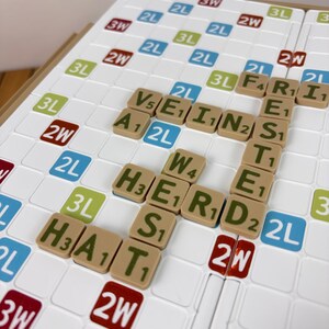 May include: A white board game grid with a grid of squares featuring colored labels like 2L, 3L, 2W, and 3W. Tan letter tiles are placed on the board forming the words VEIN, FRIESTED, HERD, and HAT, with each tile displaying a letter and a numerical value.