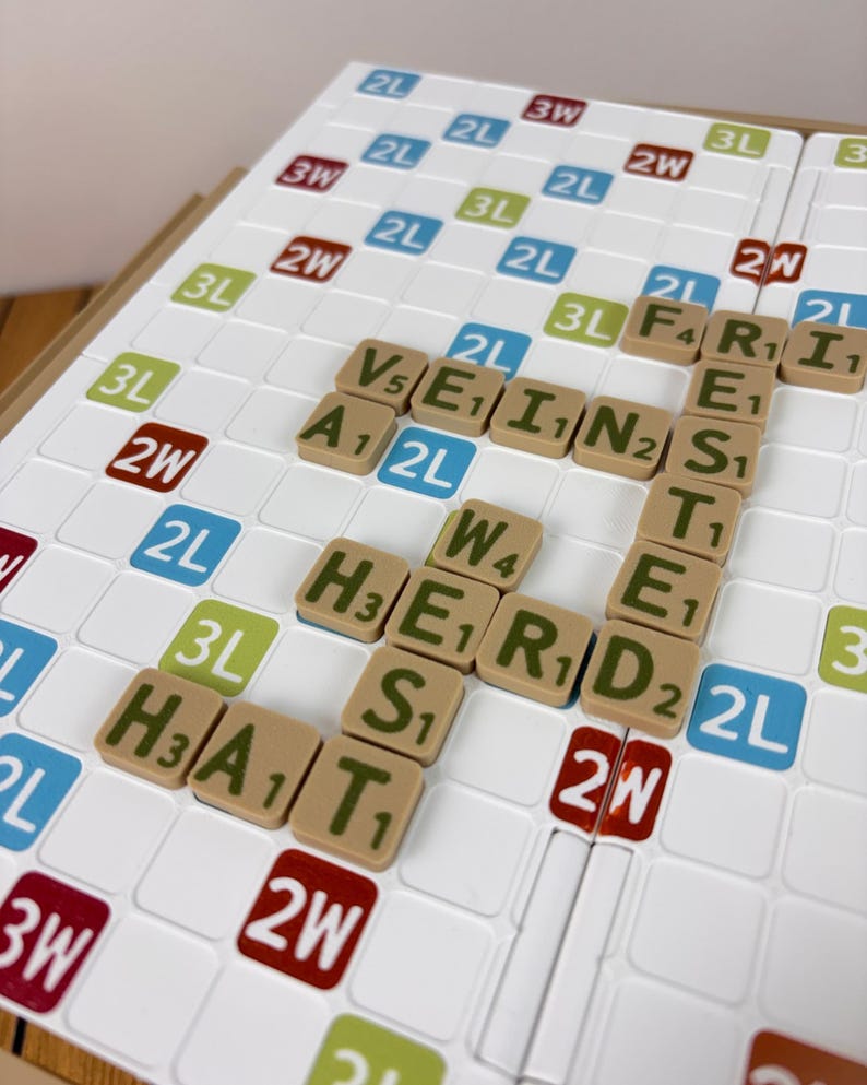 May include: A white board game grid with a grid of squares featuring colored labels like 2L, 3L, 2W, and 3W. Tan letter tiles are placed on the board forming the words VEIN, FRIESTED, HERD, and HAT, with each tile displaying a letter and a numerical value.