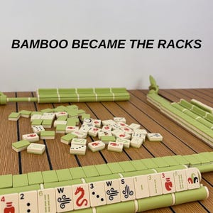 May include: A Mahjong game set featuring light green racks and tiles with red, black, and green symbols. The text BAMBOO BECAME THE RACKS is visible above the game pieces. The tiles are scattered in the center with racks positioned around them.