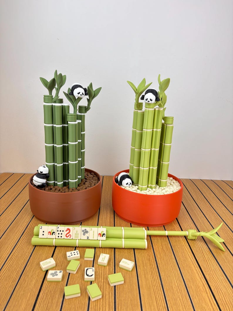 May include: Two potted bamboo plant replicas in brown and orange circular containers, each featuring small panda figures. A horizontal bamboo-shaped game piece rack holds mahjong tiles, with additional loose tiles scattered nearby.