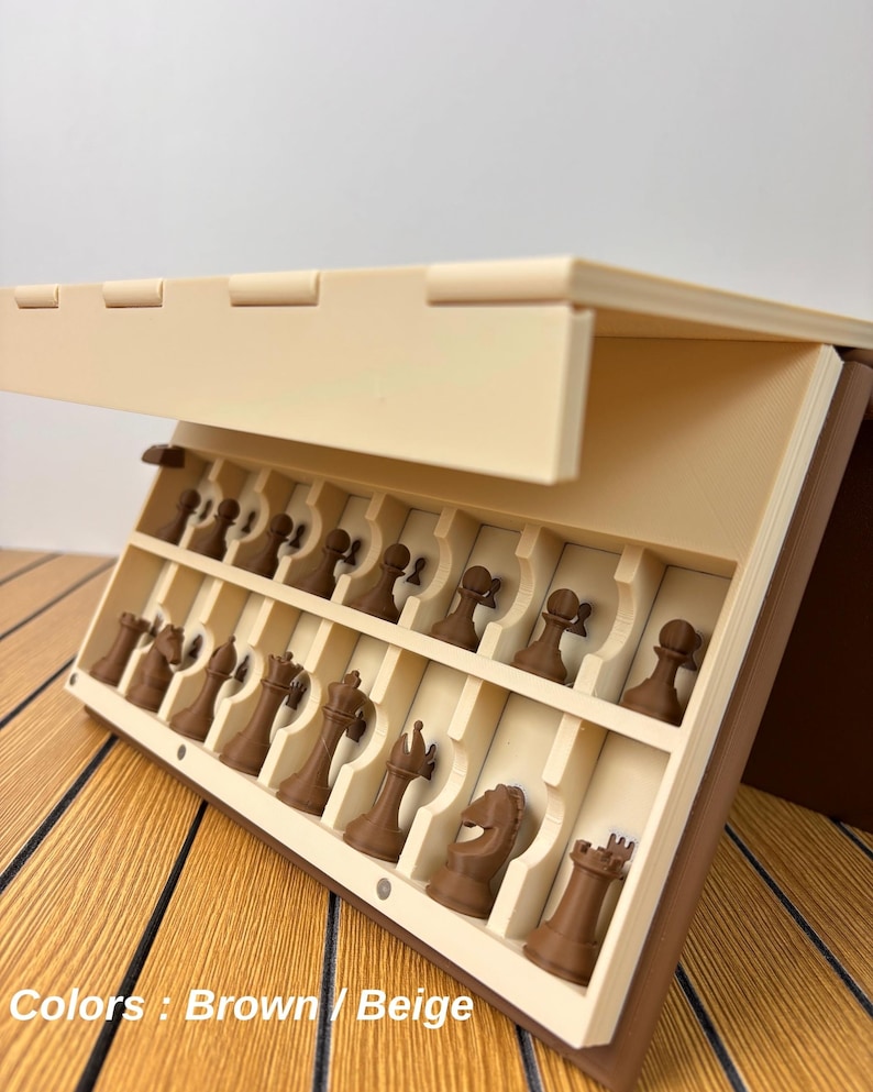 K&ouml;nnte beinhalten: Ein beigefarbenes und braunes, zusammenklappbares Schachspiel-Etui mit ge&ouml;ffnetem Deckel, das zwei innere Reihen geformter F&auml;cher enth&uuml;llt. Jedes Fach enth&auml;lt eine braune Schachfigur, darunter Bauern, Springer, Turm, L&auml;ufer und K&ouml;nig.