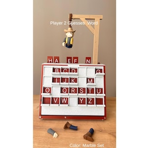 May include: A red and white word guessing game with a gallows-style structure and a small figure. The game board has letter tiles and the text "Player 2 Guesses Word." The color is described as "Marble Set."