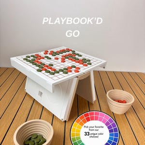 Puede incluir: Una mesa de juego blanca etiquetada como PLAYBOOK'D GO con una superficie de cuadrícula que presenta piezas de juego circulares naranjas y verdes. Dos cuencos beige acanalados contienen piezas adicionales. Un gráfico circular muestra 33 colores.