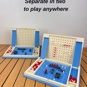 May include: A two-part strategy board game featuring a blue and cream plastic grid with the text Separate in two to play anywhere. The game includes gray miniature ships, red and white pegs for tracking hits and misses on a vertical board.