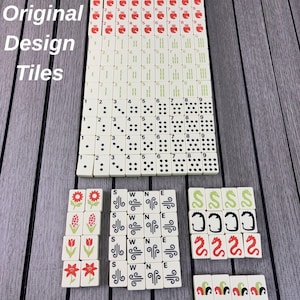 May include: A collection of off-white Mahjong tiles arranged in rows. The set includes numbered tiles in red and green, dot tiles, flower tiles, wind tiles marked S, W, N, E, and dragon tiles in green, black, and red. The text Original Design Tiles is visible.