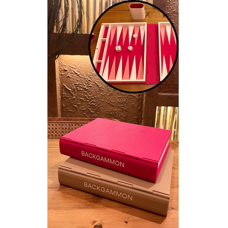 May include: A closed, hot pink backgammon game box is stacked on top of a tan backgammon game box. The text "BACKGAMMON" is printed in white on the spine of each box. The top box is open, revealing a red playing surface with white and pink triangles.