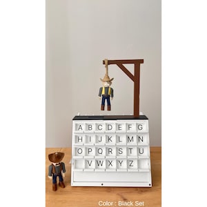 May include: A white letter board with black trim and a miniature cowboy figure hanging from a gallows. The board has slots for letters A-Z. Another cowboy figure stands to the left. The text "Color: Black Set" is at the bottom.