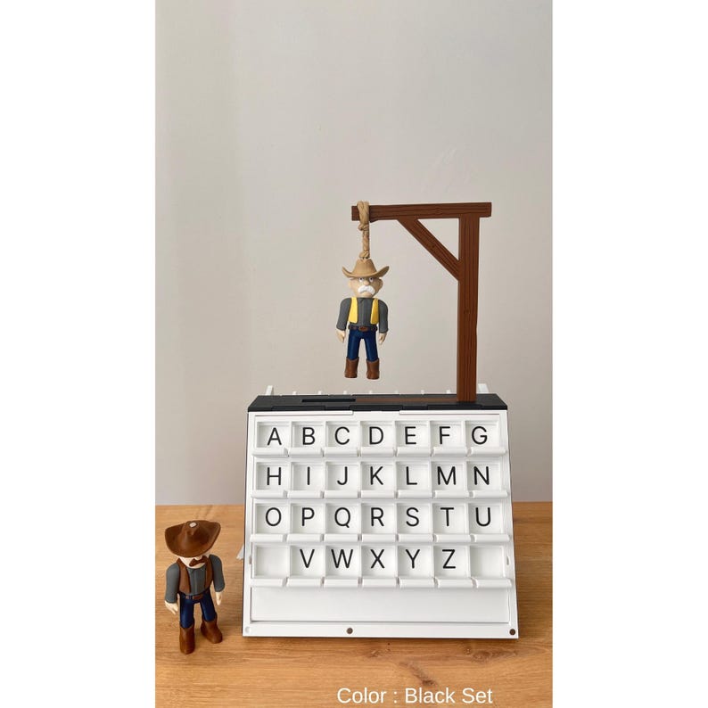 May include: A white letter board with black trim and a miniature cowboy figure hanging from a gallows. The board has slots for letters A-Z. Another cowboy figure stands to the left. The text "Color: Black Set" is at the bottom.