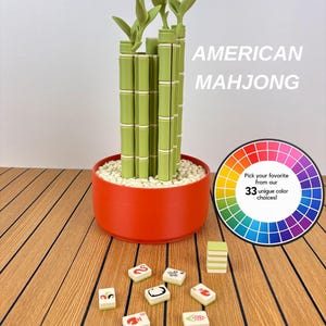 May include: A decorative bamboo plant sculpture in a round orange pot filled with white pebbles, accompanied by scattered American Mahjong tiles and a circular color wheel graphic with the text Pick your favorite from our 33 unique color choices!