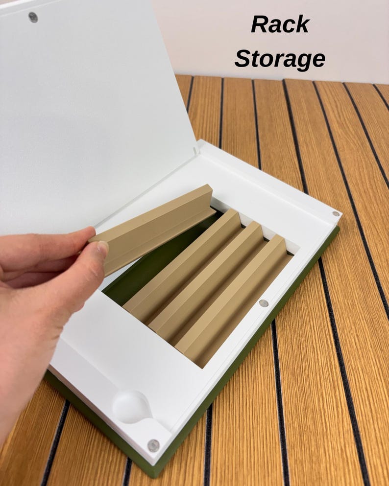 May include: A white and olive green storage case with the text Rack Storage printed on the lid. The interior features a series of tan, angled dividers designed for organizing items, with one divider being lifted by a hand.