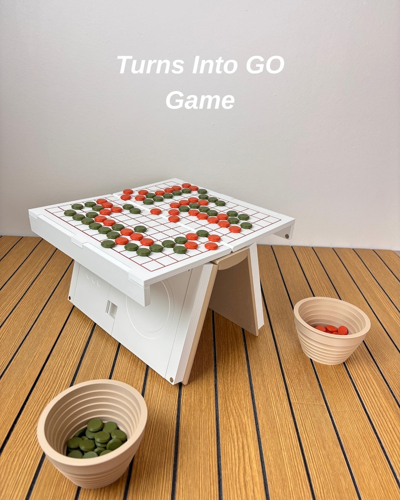 May include: A white Go game board with a red grid, featuring green and orange circular game pieces arranged on the surface. The text "Turns Into GO Game" is visible above the board. Two beige, ribbed bowls containing additional game pieces.