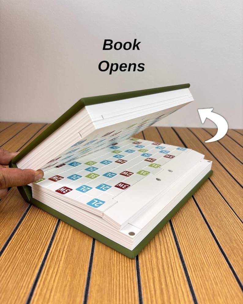 May include: A green hardcover book with the text Book Opens printed above it. The book is partially open, revealing internal pages featuring a grid of white squares with small colored labels containing the text 2L, 3W, and 2W. A white arrow icon points.