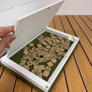 May include: A white and olive green rectangular tile storage box with a hinged lid, containing a collection of tan letter tiles with green lettering. The text Tile Storage is printed in black in the upper right corner of the image.