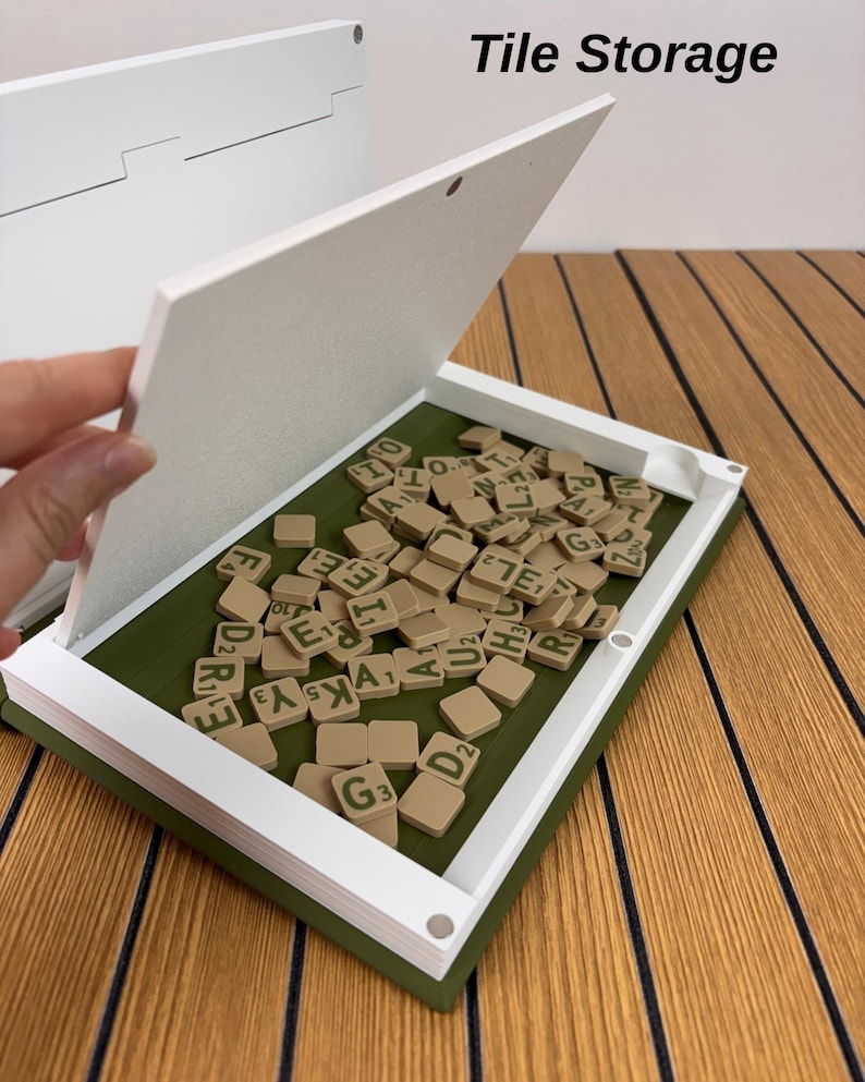 May include: A white and olive green rectangular tile storage box with a hinged lid, containing a collection of tan letter tiles with green lettering. The text Tile Storage is printed in black in the upper right corner of the image.