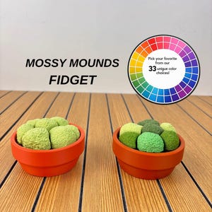 May include: Two orange terracotta pots containing textured, moss-like green mounds. Text reads: MOSSY MOUNDS FIDGET. A circular colour wheel graphic includes the text: Pick your favourite from our 33 unique colour choices!