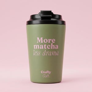 Op de afbeelding: Een olijfgroene reismok met een zwart deksel. De mok heeft de roze tekst "More matcha less drama" en "Coolby Club" eronder. Ontworpen voor warme of koude dranken.