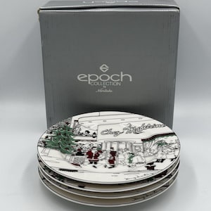 Puede incluir: Una pila de cuatro platos de cerámica blanca con un diseño Chez Madeleine en negro y rojo. Los platos presentan una escena navideña con figuras y un árbol de Navidad. Los platos son de la colección Epoch de Noritake.