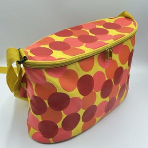 Peut inclure: Sac à déjeuner isotherme jaune avec un motif de grands cercles superposés rouges, oranges et roses. Il est doté d'une fermeture éclair et d'une bandoulière jaunes. Idéal pour transporter des aliments.