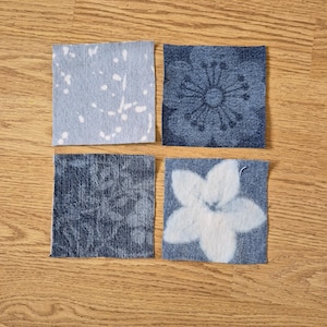 May include: Four square denim fabric patches with unique designs. One patch features a light blue background with white splatters. Another has a dark blue floral pattern. The other two patches have a dark blue floral pattern and a white flower design.