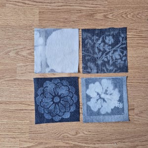May include: Four square fabric patches featuring distinct denim-style patterns. The top left shows a light blue abstract design, the top right a dark blue floral vine print, the bottom left a dark blue mandala, and the bottom right a light blue hibiscus.
