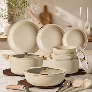May include: A kitchen cookware set in a speckled cream finish featuring multiple pots and pans with light wood-toned detachable handles, glass lids with gold-tone knobs, and matching silicone kitchen utensils including a spatula and ladle.