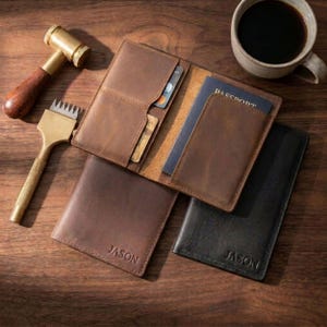 May include: Two leather passport holders, one brown and one black, each embossed with the name JASON. The brown holder is open, revealing interior card slots and a blue passport. A brass mallet and a leather stitching tool are placed nearby.