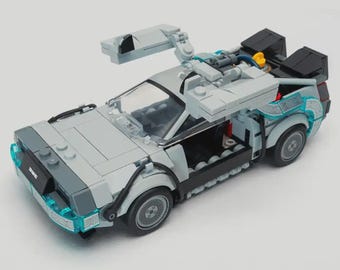 May include: A gray plastic building block model of a sports car with gull-wing doors that open upward. The vehicle features black trim, translucent blue light accents on the front and rear fenders, and a small DMC logo on the front bumper.