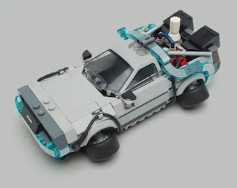 May include: A gray plastic building block model of a sports car featuring a transparent windshield, black wheels, and translucent blue light accents along the front and rear. The rear section includes a white cylindrical component and black vents.