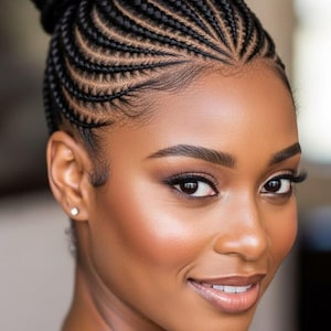 Può includere: Una persona dalla pelle scura e occhi marroni con un'acconciatura a chignon alto caratterizzata da intricate trecce aderenti nere che si irradiano dalla sommità del capo. Presenta sopracciglia definite, trucco occhi leggero e un piccolo orecchino.