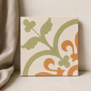 May include: Square ceramic tile with a cream background and a repeating floral pattern in shades of green and orange. The design features stylized leaves and curved lines, creating a decorative element. The tile is suitable for home decor.
