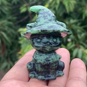May include: A small, carved stone figurine of a cat wearing a pointed witch hat. The sculpture features a mottled pattern of dark forest green and black throughout the entire surface, with a smooth, polished texture and defined facial features.