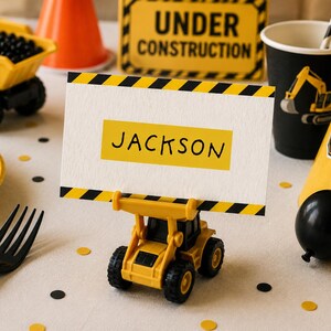 Op de afbeelding: Een verjaardagsfeest met bouwthema in geel en zwart. Met een naamkaartje met "JACKSON", een speelgoedgraafmachine, feesthoeden en een bord met "UNDER CONSTRUCTION". Decoraties zijn onder meer confetti en een zwarte vork.