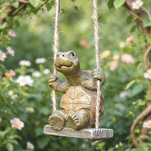 Puede incluir: Un adorno de jardín caprichoso con una figura de tortuga en un columpio. La tortuga, con una expresión sonriente, está suspendida de un arco cubierto de vid con cuerdas. La escultura se encuentra sobre un fondo de vegetación y flores.
