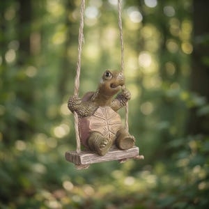 Puede incluir: Un adorno de jardín caprichoso que representa una tortuga sonriente en un columpio. La tortuga es verde y marrón, con un caparazón detallado y piel texturizada. El columpio es de madera y cuerda, creando una encantadora decoración exterior.