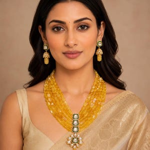 Peut inclure: Un collier à plusieurs rangs composé de perles jaunes translucides, d'une rangée centrale verticale de trois pierres blanches carrées à bordure verte, et d'un pendentif floral avec des pierres blanches et une goutte jaune. Boucles d'oreilles assorties.