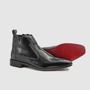 May include: A black ankle boot with a textured snakeskin pattern, a side zipper closure, a pull tab at the heel, and a distinct red sole. The boot features a low block heel and a pointed toe design, showcasing a glossy finish on the exterior surface.