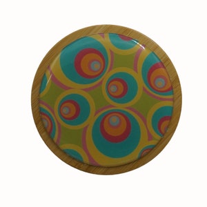 May include: A round wooden coaster featuring a colourful, abstract design of overlapping circles in shades of blue, green, pink, orange, and yellow.