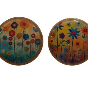 May include: Two round wooden coasters with colorful floral designs. The coasters feature a variety of flowers in shades of blue, red, yellow, and orange.
