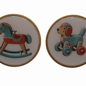 May include: Two round decorative coasters with a wooden rim. One coaster features a teal and red rocking horse illustration. The other coaster has a teal and red dog toy illustration. Both illustrations are on a white background.