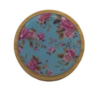 Puede incluir: Un posavasos redondo de madera con un diseño floral azul y rosa. El posavasos tiene un acabado brillante y es perfecto para proteger las superficies del calor y los derrames.